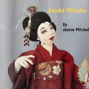 May include: A handmade doll dressed in a red and black kimono with a floral pattern. The doll is holding a fan and has a traditional Japanese hairstyle with a decorative hairpiece. The doll is titled "Geisha Mitsuko" and is by "sharon Mitchell".