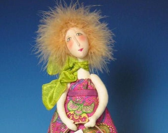 May include: A handmade doll with blonde hair, wearing a pink and green dress, holding a brown and pink tote bag. The doll is sitting on a purple suitcase with colorful straps.