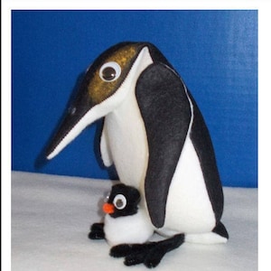 May include: Two felt penguin toys, one large and one small. The larger penguin is white with black wings and a black beak. The smaller penguin is white with black wings and a black beak. Both penguins have black eyes.