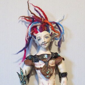 May include: A handmade doll with a black tail, red and blue hair, and a leather outfit. The doll is holding a trident and a red fish.