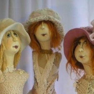 May include: Three handmade dolls with different colored hats and lace dresses. The dolls have painted faces and red, blonde, and brown hair.