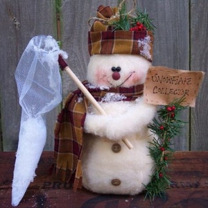 Könnte beinhalten: Ein Schneemann mit einem karierten Hut und Schal hält ein Netz und ein Schild mit der Aufschrift "Schneeflocken-Sammler".