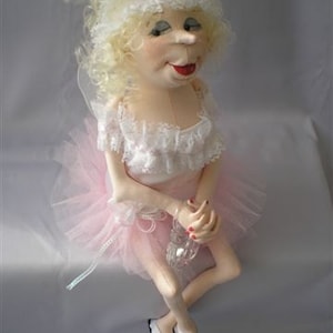 Peut inclure: Une poupée faite à la main portant un tutu rose, un haut en dentelle blanche et des chaussures blanches. La poupée a des cheveux blonds bouclés et une expression fantaisiste.