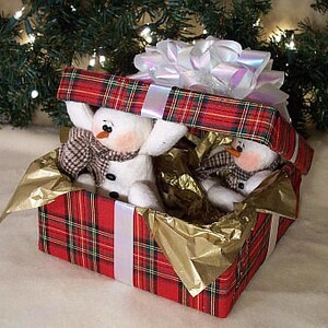 Könnte beinhalten: Zwei weiße Schneemann-Figuren mit schwarzen Augen und Knöpfen schauen aus einer roten und grünen karierten Geschenkbox mit einem weißen Satinband und einer weißen Schleife. Die Box ist mit goldenem Seidenpapier gefüllt.