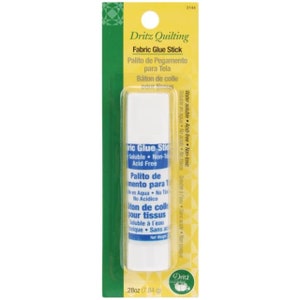 May include: A white fabric glue stick with blue text that reads "Fabric Glue Stick" and "Water soluble - Acid-free - Non-toxic". The glue stick is packaged in a yellow and green wrapper with the Dritz Quilting logo.