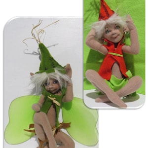 Könnte beinhalten: Zwei handgefertigte Filz-Feenpuppen mit grünen Flügeln und spitzen Hüten. Eine Puppe sitzt mit gekreuzten Beinen und die andere kniet mit gekreuzten Armen.