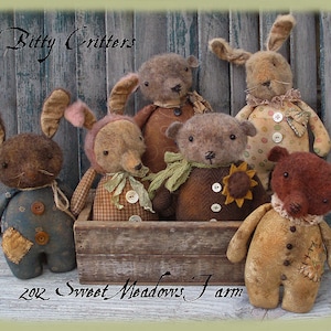 以下が含まれることがあります： 木製の箱の中に、ウサギ、クマ、キツネなど、手作りのぬいぐるみ6体が座っています。おもちゃはさまざまな生地で作られており、素朴でヴィンテージな外観をしています。おもちゃはそれぞれ異なる服装をしていて、個性的な個性を持っています。箱には「2012 Sweet Meadows Farm」とラベルが貼られています。