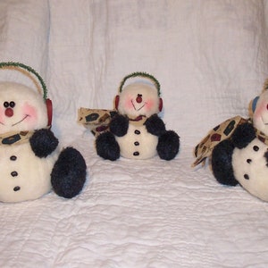 May include: Three handmade snowman ornaments with green and blue earmuffs, black felt arms, and a brown and white patterned scarf.