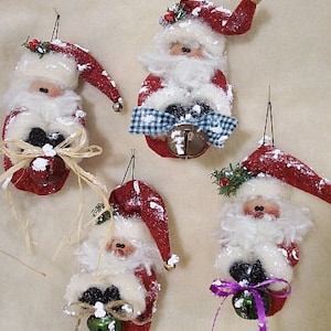 Könnte beinhalten: Vier handgefertigte Weihnachtsbaumschmuck aus Filz, die den Weihnachtsmann darstellen. Jeder Schmuckstück hat einen weißen Bart, einen roten Hut und eine Glocke. Die Schmuckstücke sind mit weiß-blauem kariertem Stoff, grünen Zweigen und einer braunen Schleife verziert.
