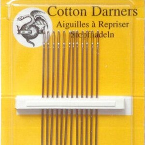 May include: A package of John James Cotton Darners needles, size 7, containing 12 needles. The packaging is yellow and clear, with text in English and French. The needles are held in a white plastic holder.