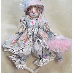 May include: A handmade doll with a bunny head, wearing a blue and pink floral dress with lace trim, a pink and blue hat, and holding a pink feathered hat.