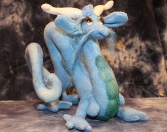 May include: A blue and green plush dragon with a long, curled tail and a white horn. The dragon has a friendly expression and is made of soft, fuzzy fabric.