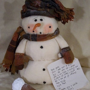 Könnte beinhalten: Eine handgemachte Schneemann-Puppe mit einem braunen und weißen karierten Schal und Hut. Der Schneemann hält ein handgeschriebenes Notiz, auf dem steht: "Lieber Weihnachtsmann, da ich dieses Jahr brav war, darf ich bitte eine neue Rose, einen Knopf und ein Stück Srite haben! Ich möchte auch ein neues Paar Fäustlinge! Danke! Liebe Grüße, Flocke"