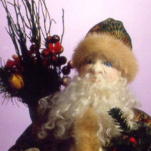 Op de afbeelding: Een close-up van een handgemaakte kerstmanpop met een witte baard en een bontkraag. De pop draagt een groen-gouden gepatroneerde jurk en houdt een takje groen met rode bessen vast.
