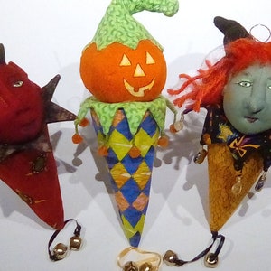 May include: Three handmade Halloween ornaments shaped like cones with different characters on top. The first ornament has a red devil face, the second has a pumpkin face, and the third has a witch face with red hair.
