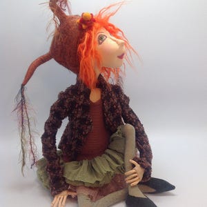 May include: A handmade doll with red hair, a brown hat, and a green skirt. The doll is sitting with its legs crossed and wearing black shoes.