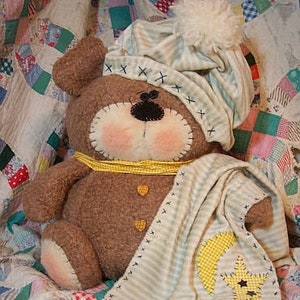 May include: A brown teddy bear wearing a striped sleep cap and a blanket with a yellow star and moon design. The bear is sitting on a patchwork quilt.