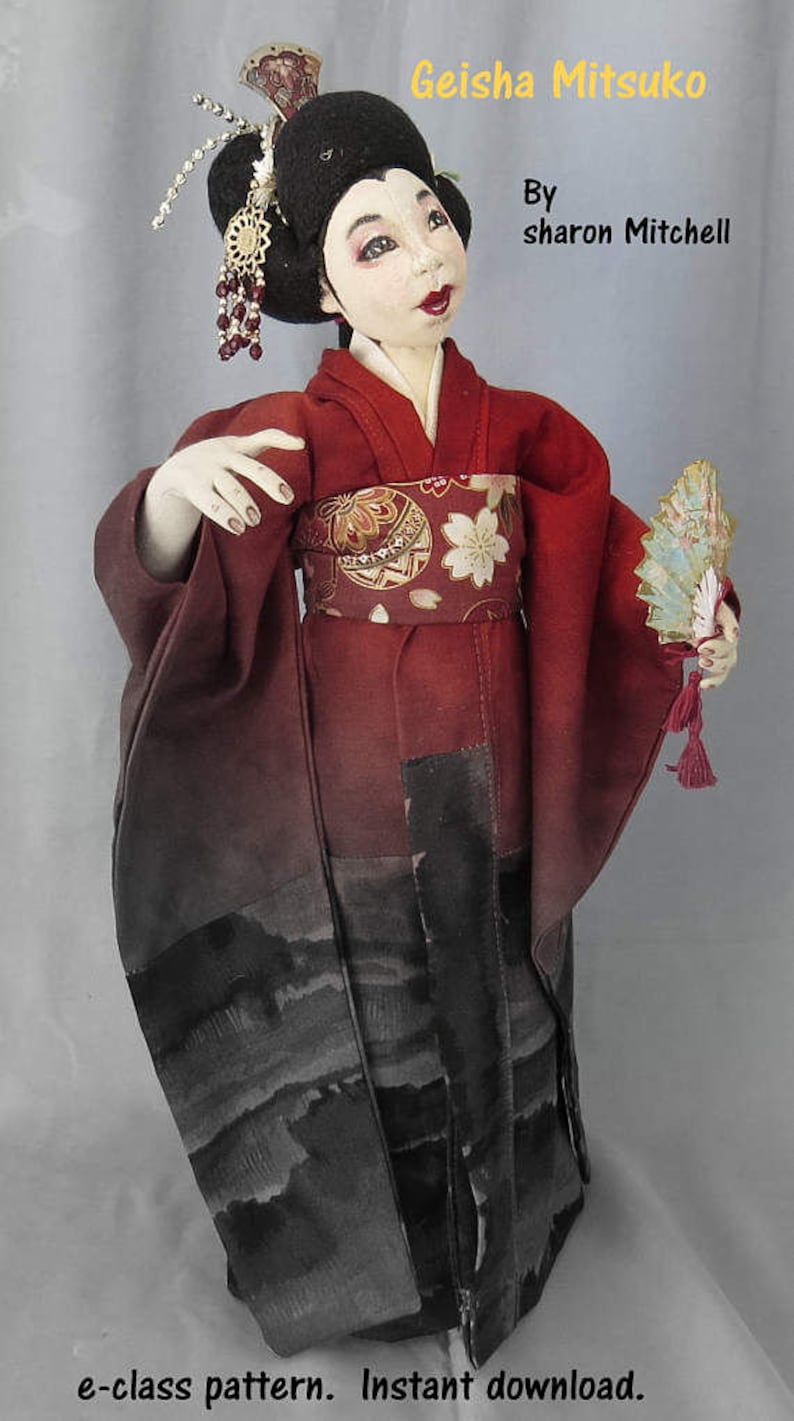 May include: A handmade doll dressed in a red and black kimono with a floral pattern. The doll is holding a fan and has a traditional Japanese hairstyle with a decorative hairpiece. The doll is titled "Geisha Mitsuko" and is by "sharon Mitchell".