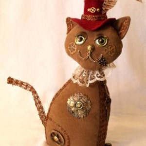 Könnte beinhalten: Eine braune Plüschkatze, die einen roten Hut mit einer Feder, einen weißen Spitzenkragen und verschiedene Verzierungen im Steampunk-Stil trägt, darunter Zahnräder und Ketten.