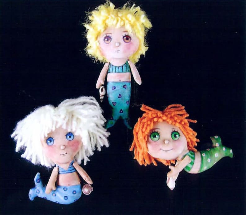 May include: Three handmade fabric dolls dressed as mermaids. The dolls have yarn hair and painted faces. One doll has blonde hair and a blue and white tail, another has white hair and a blue tail, and the third has red hair and a green tail.