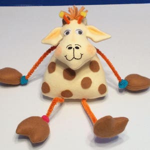 May include: A plush giraffe toy with brown spots, orange pipe cleaner legs, and blue and pink accents. The giraffe has a smiling face with large eyes.