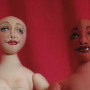 Puede incluir: Dos muñecas de tela hechas a mano con caras pintadas. La muñeca de la izquierda tiene un tono de piel claro y ojos azules. La muñeca de la derecha tiene un tono de piel marrón y ojos marrones.