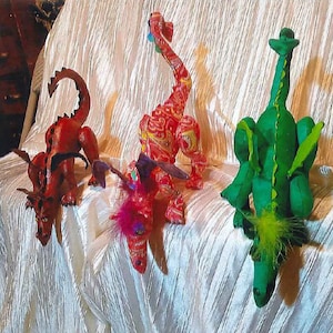 May include: Three plush dragon toys, one red, one green, and one red with pink and purple accents. The dragons are all in different poses, with their heads and tails raised.