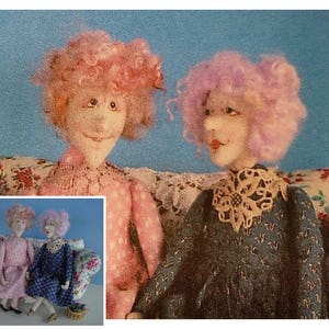 May include: Two handmade dolls with pink and purple yarn hair sitting on a floral patterned couch. The dolls are wearing dresses with lace details.