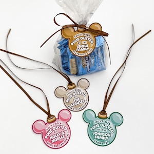 May include: A clear plastic bag filled with blue-wrapped chocolates, tied with a brown ribbon and a mouse-ear shaped tag reading You've Been Pixie Dusted By The Snow Family Stateroom 11025, alongside three additional mouse-ear tags.