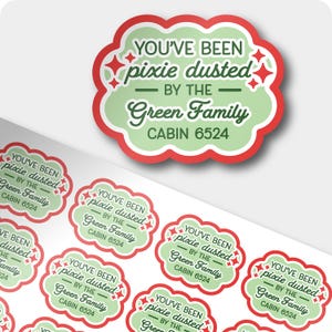 May include: A sheet of scalloped-edge stickers featuring a light green center with a red border. The text reads: YOU'VE BEEN pixie dusted BY THE Green Family CABIN 6524, accented with small red four-pointed star icons.