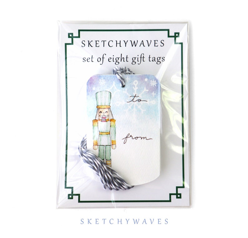 May include: A set of eight watercolor gift tags featuring a nutcracker illustration with a snowflake background. The tags are white with a blue, purple, and green watercolor wash. The tags have the words "to" and "from" printed on them.