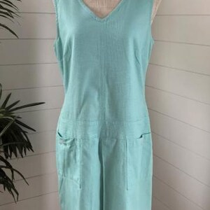 May include: A sleeveless, light blue, linen dress with a v-neck and two pockets on the front.