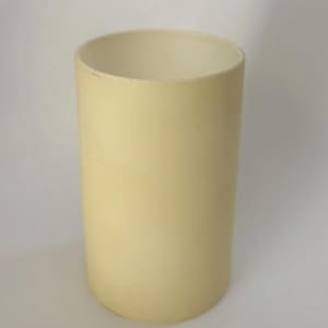 May include: A cylindrical, pale cream-colored vessel with a smooth, matte finish. The object features a simple, open-top design with straight vertical walls and a flat base, presenting a clean, uniform appearance throughout its entire structure.