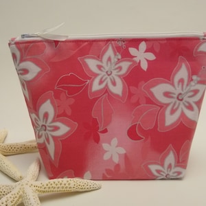 May include: A pink zippered pouch with a white floral print. The pouch is made of fabric and has a white zipper.