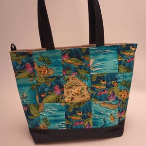 May include: A patchwork tote bag featuring a tropical turtle design. The bag has a dark blue base and straps, with a vibrant pattern of turtles, islands, and ocean scenes in shades of blue, green, and coral. The bag is designed for carrying items.