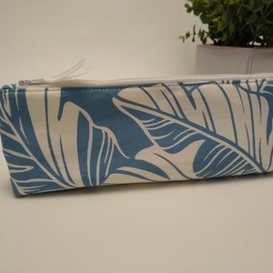 May include: A rectangular pencil case with a white zipper and pull tab. The case features a blue background with a white tropical leaf pattern. The case is approximately 8 inches long.