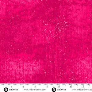 May include: A bright fuchsia fabric with a textured, distressed look. The fabric has vertical brushstroke patterns and scattered white speckles, creating a dynamic visual effect. The bottom edge displays a ruler with inch measurements and the Andover Fabrics logo.