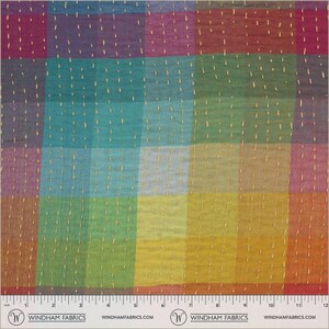 May include: A multicolored fabric featuring a grid of squares in shades of red, purple, blue, green, and yellow. The textile is accented with vertical rows of light-colored running stitches. A ruler at the bottom shows a 12-inch scale.