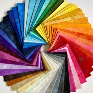 May include: A vibrant display of fabric swatches arranged in a spiral, showcasing a spectrum of colors. The swatches range from deep blues and purples to bright greens, yellows, oranges, and reds. The arrangement highlights the variety of textures and hues available.