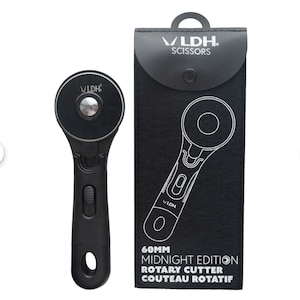 Pode incluir: Cortador rotativo preto com uma lâmina de 60 mm, etiquetado como "60MM MIDNIGHT EDITION ROTARY CUTTER COUTEAU ROTATIF" e "VLDH SCISSORS".