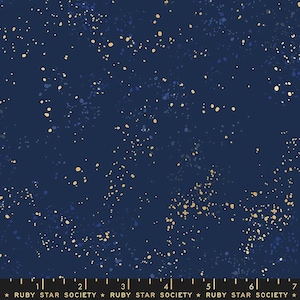 Op de afbeelding: Donker marineblauwe stof met een gespikkeld patroon van gouden en blauwe stippen, dat lijkt op een sterrenhemel. De stof heeft een subtiele glans en is geschikt voor diverse naaiprojecten. De tekst "RUBY STAR SOCIETY" staat onderaan.