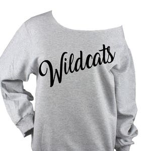 May include: Gray off-the-shoulder sweatshirt with the word "Wildcats" printed in black cursive lettering.