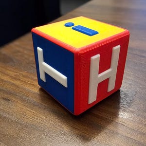May include: A red, yellow and blue cube with the letters 'I', 'H' and 'T' printed on the sides. The cube is made of plastic and has a textured surface.