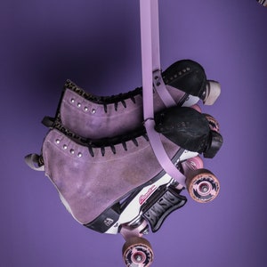 May include: A pair of purple roller skates with black wheels and a pink leopard print on the boot. The skates are hanging from a lavender strap.