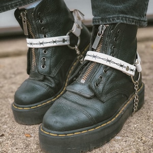 May include: Black leather platform boots with white barbed wire ankle straps and silver chain accents.