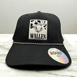 Op de afbeelding: Zwarte baseballcap met een zilveren kralenketting en een vierkante patch met een stierschedelontwerp en de naam "WALLEN". De pet heeft een gebogen klep en een "ADULT HAT" sticker.