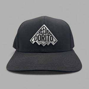 Peut inclure: Casquette de baseball noire avec une visière plate. Le chapeau présente un motif argenté et blanc d'une chaîne de montagnes avec les mots "FREEDOM DORITO" dans une police stylisée. Le chapeau est fait d'un matériau durable.