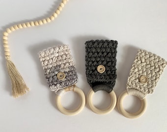 May include: Three handmade crochet ring holders in neutral tones. Each holder features a wooden ring and a button closure. The crochet work includes a gradient of gray and white, a solid dark gray, and a light beige.