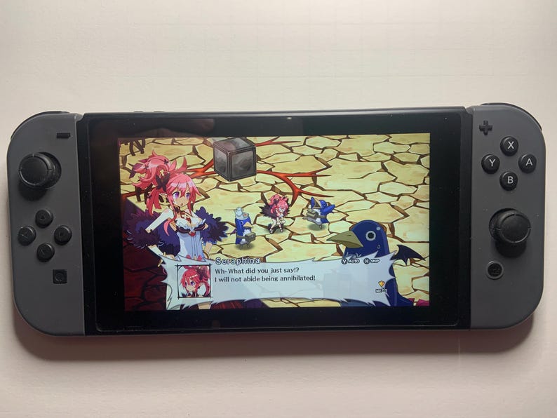 Puede incluir: Una consola Nintendo Switch gris con un juego en la pantalla. El juego presenta personajes de estilo anime y el texto "Seraphina: &iexcl;&iquest;Qu&eacute; acabas de decir!? &iexcl;No tolerar&eacute; ser aniquilada!"