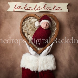 May include: A newborn baby wearing a red Santa hat and a red swaddle is sleeping in a wooden heart-shaped bowl. The bowl is being held by a pair of Santa Claus hands with white gloves. A banner above the bowl reads "fa la la la la".